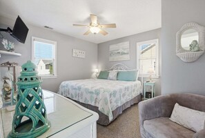A bedroom with a bed, a ceiling fan, a TV, and a window with blinds.