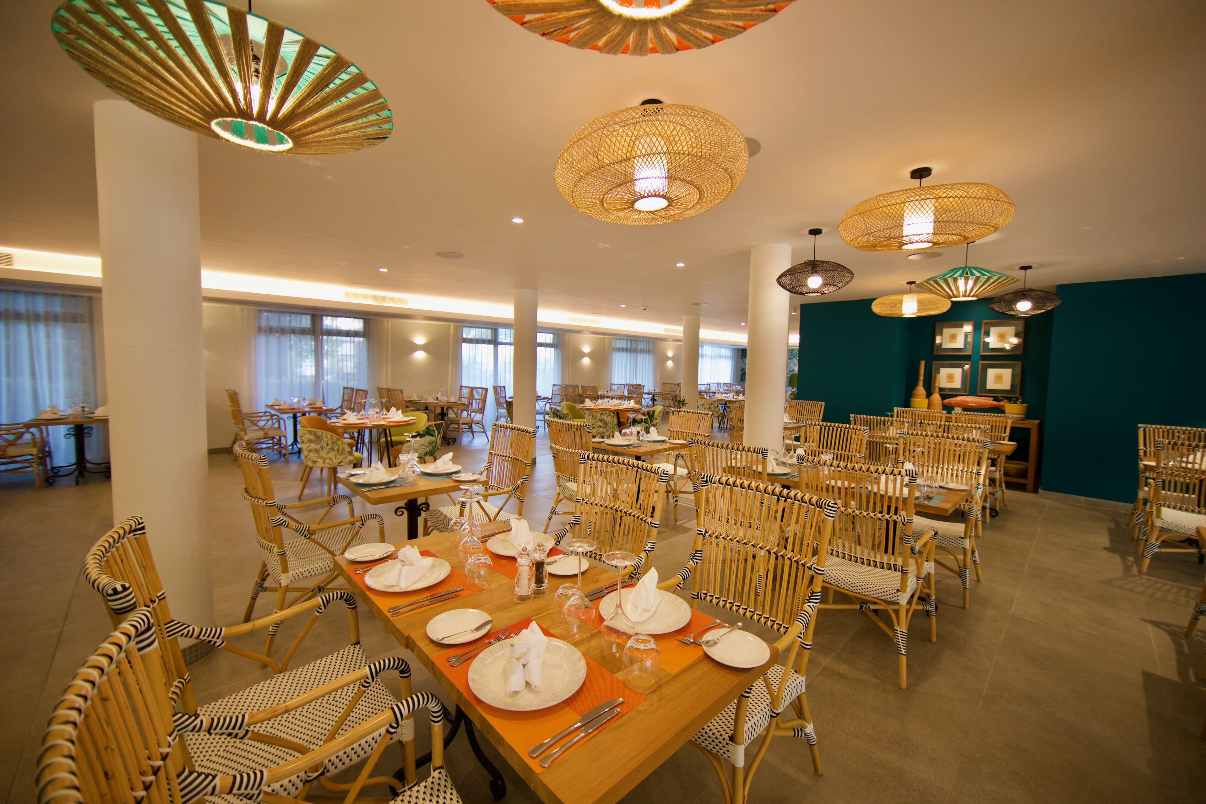 A spacious dining area with multiple tables and chairs, large windows, and decorative hanging lamps.