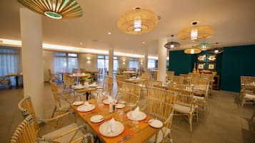 A spacious dining area with multiple tables and chairs, large windows, and decorative hanging lamps.