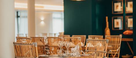 A dining area with wicker chairs and tables set for a meal, featuring hanging pendant lights and framed artwork on the wall.
