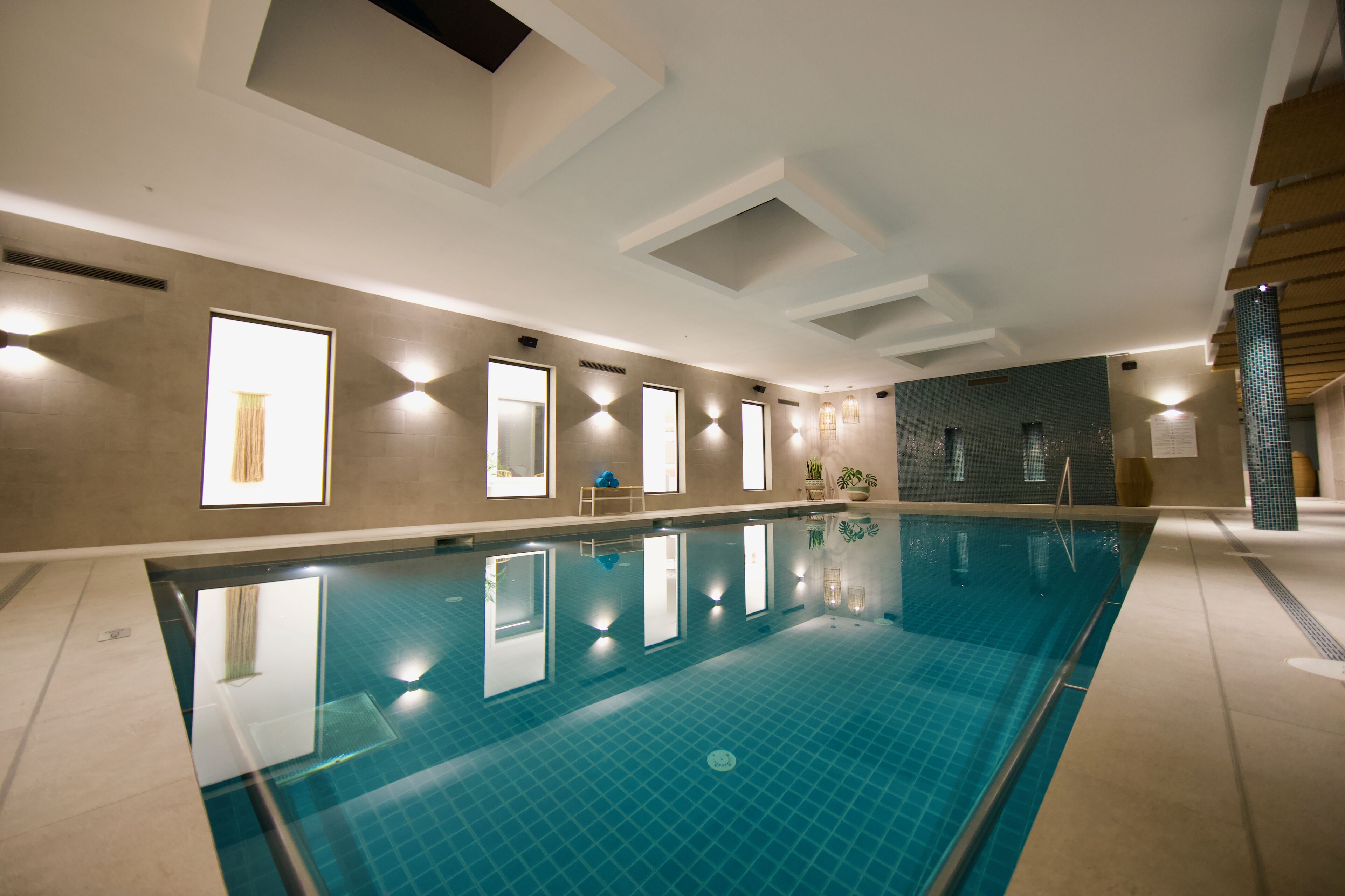Une grande piscine intérieure à l’eau d’un bleu limpide, entourée de murs ornés d’œuvres d’art encadrées et dotée d’un éclairage encastré.