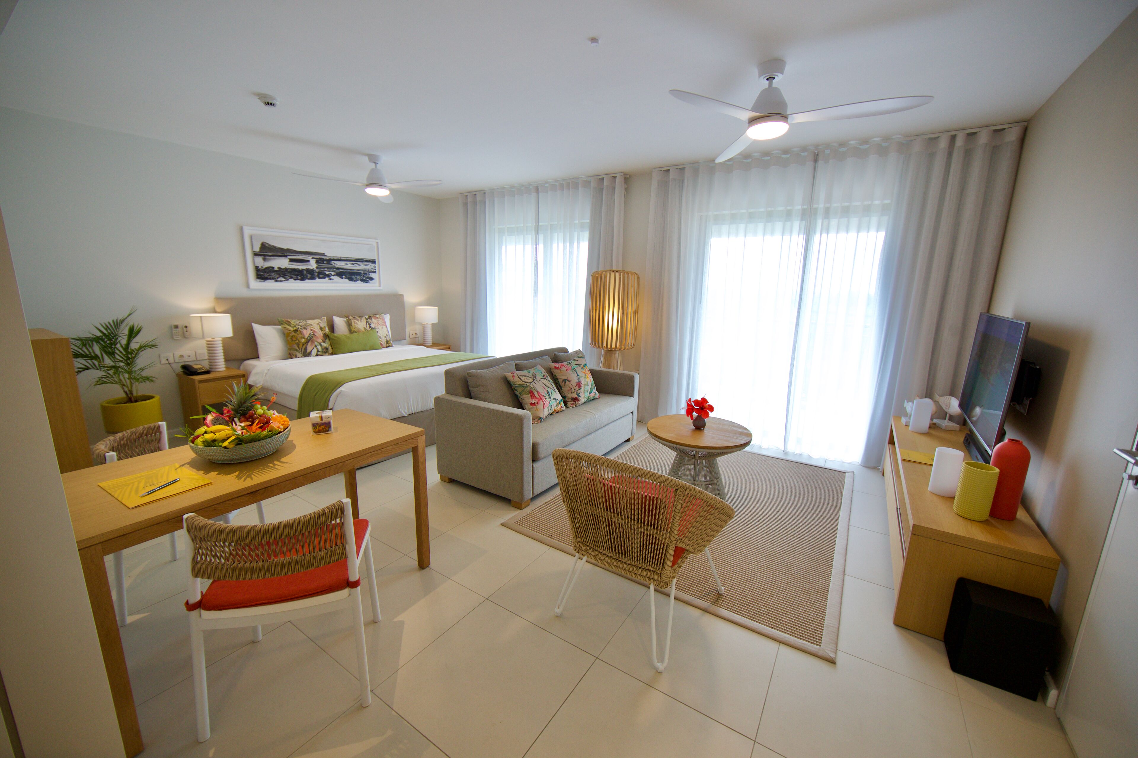 Habitación de hotel con cama, sofá, mesa de comedor, sillas, televisor y ventilador de techo.