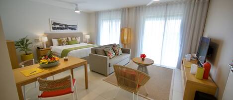 Habitación de hotel con cama, sofá, mesa de comedor, sillas, televisor y ventilador de techo.