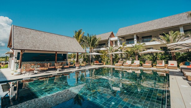 A pool area with lounge chairs and umbrellas, a covered seating area, and a building with a tiled roof. - Domaine de Grand Baie (Mont Choisy)