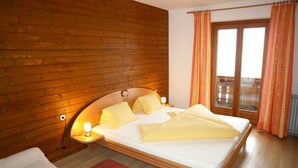 Een slaapkamer met een houten wand, een bed met geel beddengoed, een nachtkastje met een lamp en een raam met gordijnen.
