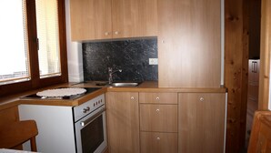 Een kleine keuken met houten kastjes, een fornuis en een spoelbak.