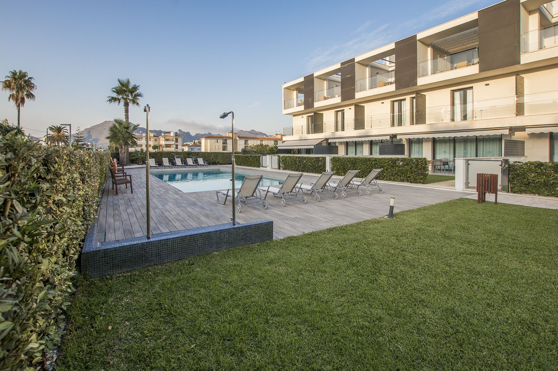 A modern hotel with a swimming pool, lounge chairs, and a well-maintained lawn.