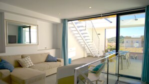En moderne stue med sofa, glasgelænder og udsigt til en trappe, der fører til en balkon.
