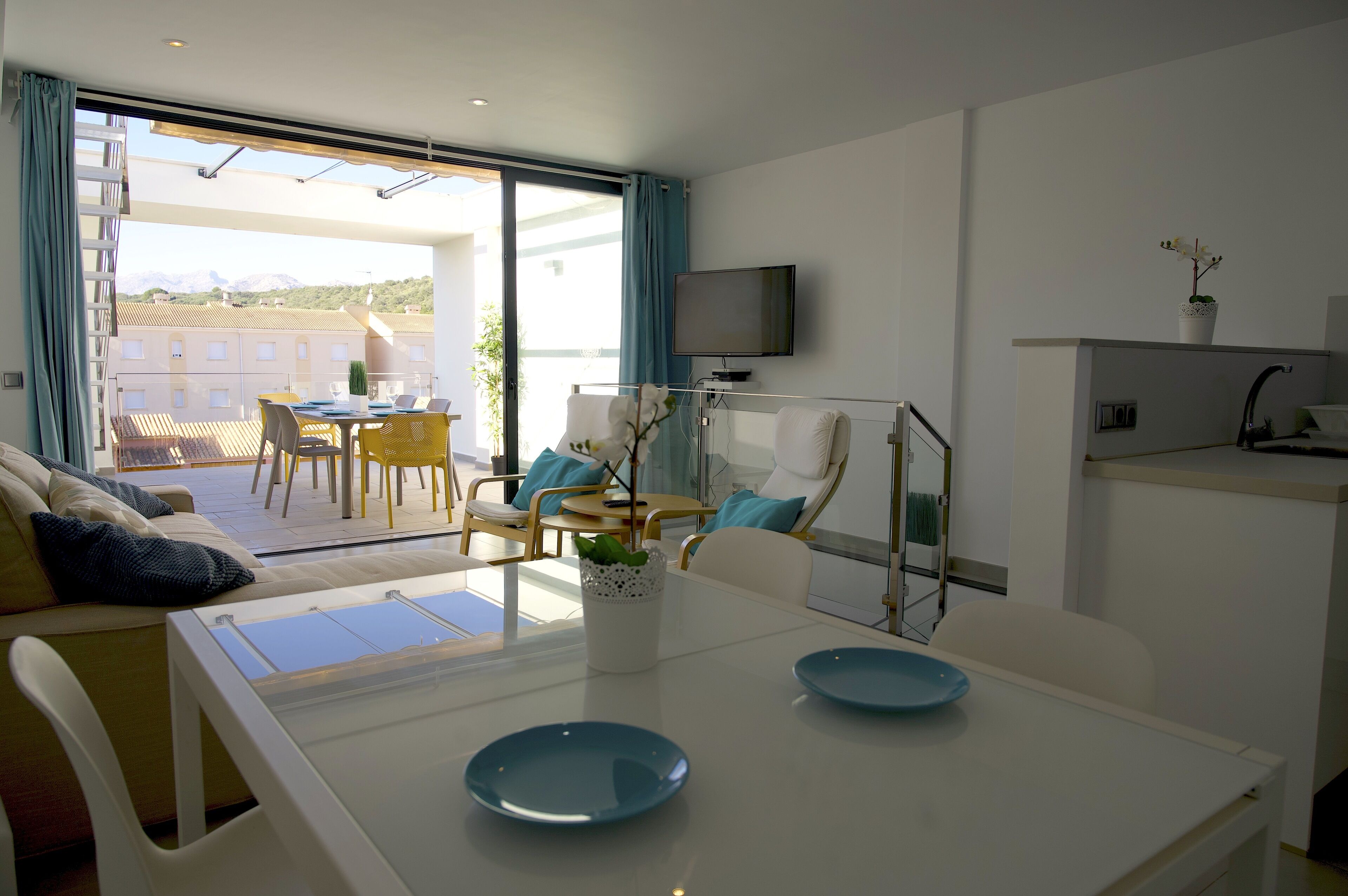 A modern hotel room with a balcony, a dining area, and a TV.