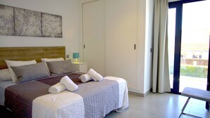 Et hotelværelse med en stor seng, et træsengegærde, et natbord, en bænk og udsigt til det fri via en skydedør.