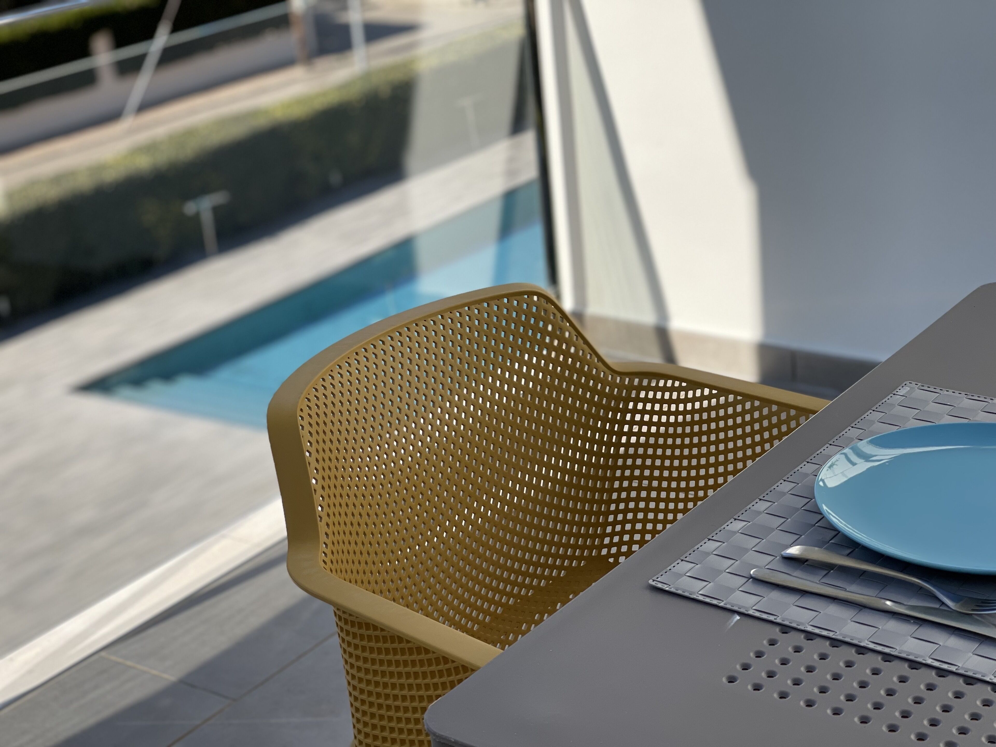 En matplats med ett bord dukat för två personer, en gul, flätad stol och utsikt över en swimmingpool.