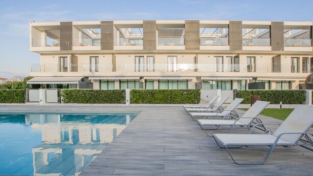 Et moderne hotel med poolområde, liggestole og en bygning med flere etager og altaner.