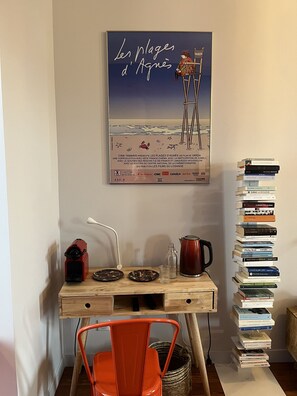 Una habitación con un escritorio de madera, una silla roja, un cartel de 'Les Plages d'Agnes' y una pila de libros.