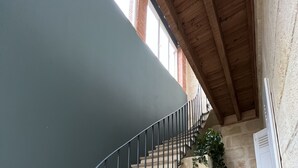 Una scala con ringhiera in metallo che conduce a un pianerottolo con una porta e una piccola sedia di legno.
