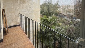 Un balcone con pavimento in legno e ringhiera nera, che si affaccia su un giardino con diverse piante e alberi.