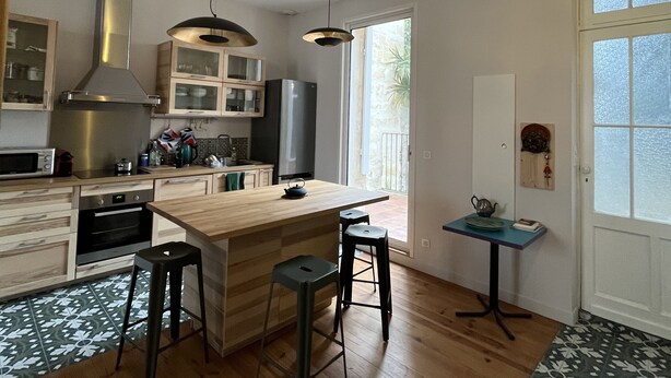 Una cucina moderna con un'isola centrale, sgabelli da bar, un tavolino con una teiera e vista all'esterno.