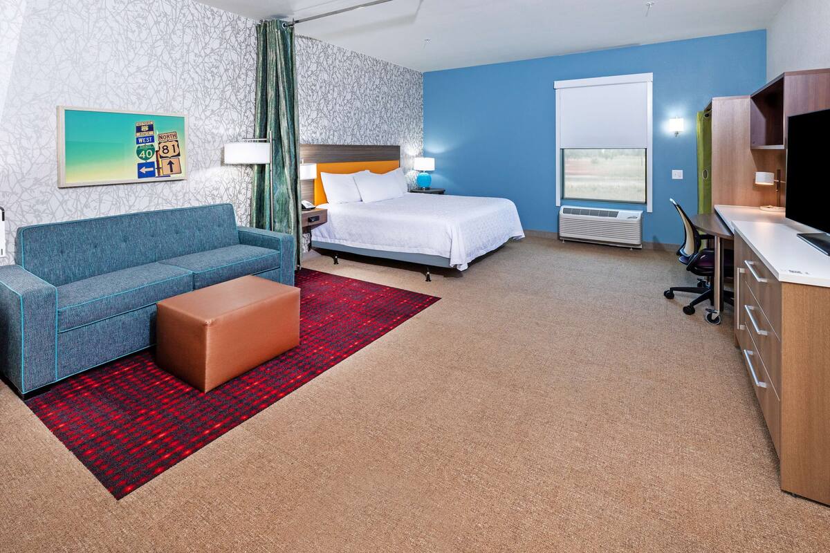 A hotel room with a bed, a sofa, a desk, and a TV.