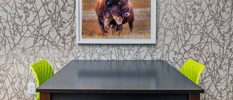 A dining table with two chairs, a framed picture of a bison, and a wall with a branch pattern.