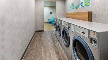 A laundry room with a row of front-loading washers and dryers, a wooden bench, and a blue chair.