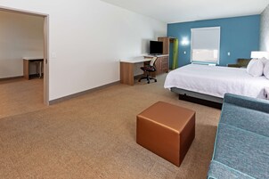 Una habitación de hotel con una cama, un escritorio con computadora, una silla, un reposapiés marrón y un sofá azul.