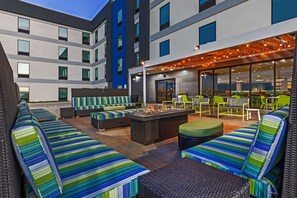 A modern outdoor lounge area with striped seating, a fire pit, and a covered patio with string lights. - Home2 Suites by Hilton Weatherford (Weatherford)