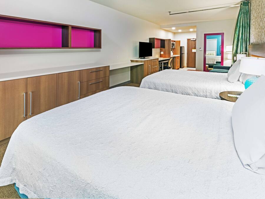 Camera d'albergo con due letti, una scrivania, un televisore e bagno visibile tramite una porta aperta.