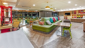 Un área de descanso moderna con un sofá verde, mesas y sillas de madera.