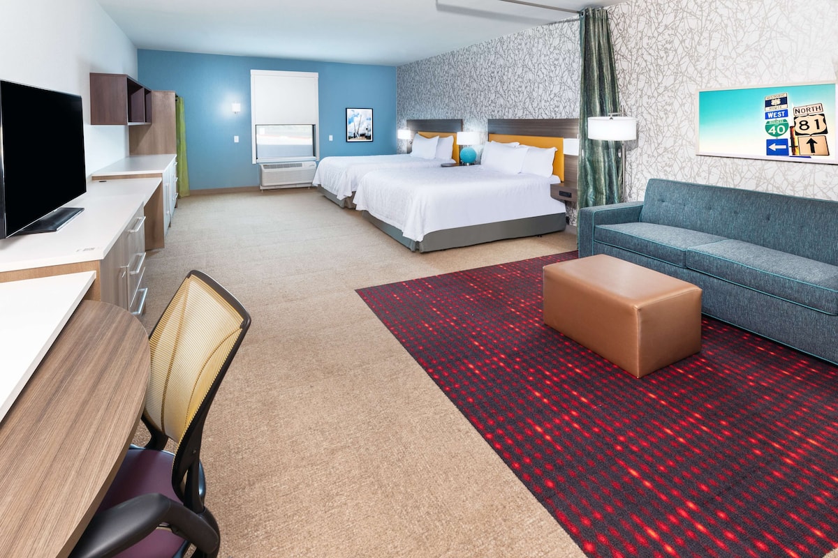 A hotel room with a bed, a sofa, a desk with a computer, a TV, and a window.