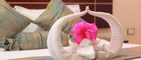Una cama bien hecha con una almohada decorativa con forma de cisne y un lazo rosa.
