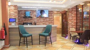 A bar area with a counter, two bar stools, a television mounted on a brick wall, and a fire extinguisher on the wall. - Vicmark Hotel Nakuru (Nakuru)