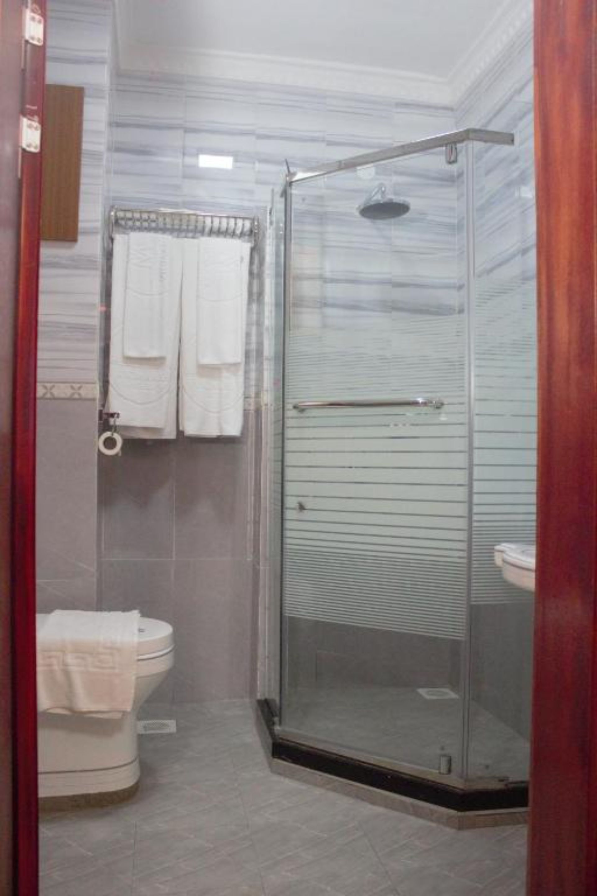 A glass-enclosed shower with a glass door, a toilet with a towel on it, and a towel rack with two towels.