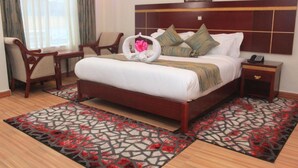 A hotel room with a wooden bed, a desk, two chairs, a nightstand, and a patterned rug. - Vicmark Hotel Nakuru (Nakuru)