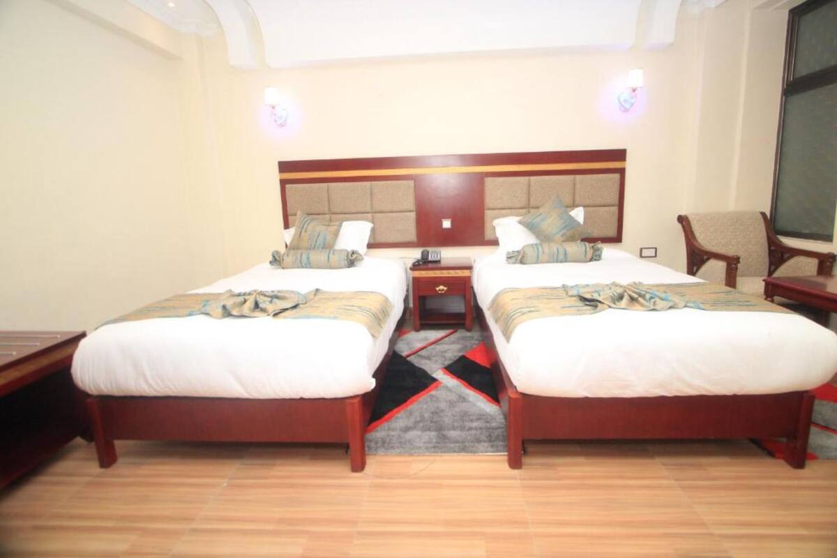 A hotel room with two beds, a nightstand, a chair, and a large window.