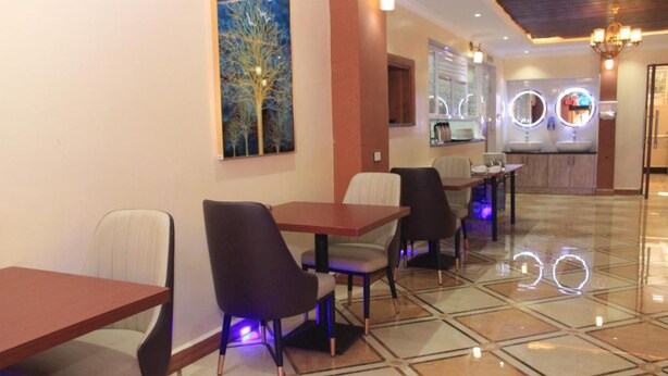 A hotel lobby with a dining area featuring tables and chairs, a kitchen area with a sink and mirror, and a painting of a tree on the wall. - Vicmark Hotel Nakuru (Nakuru)