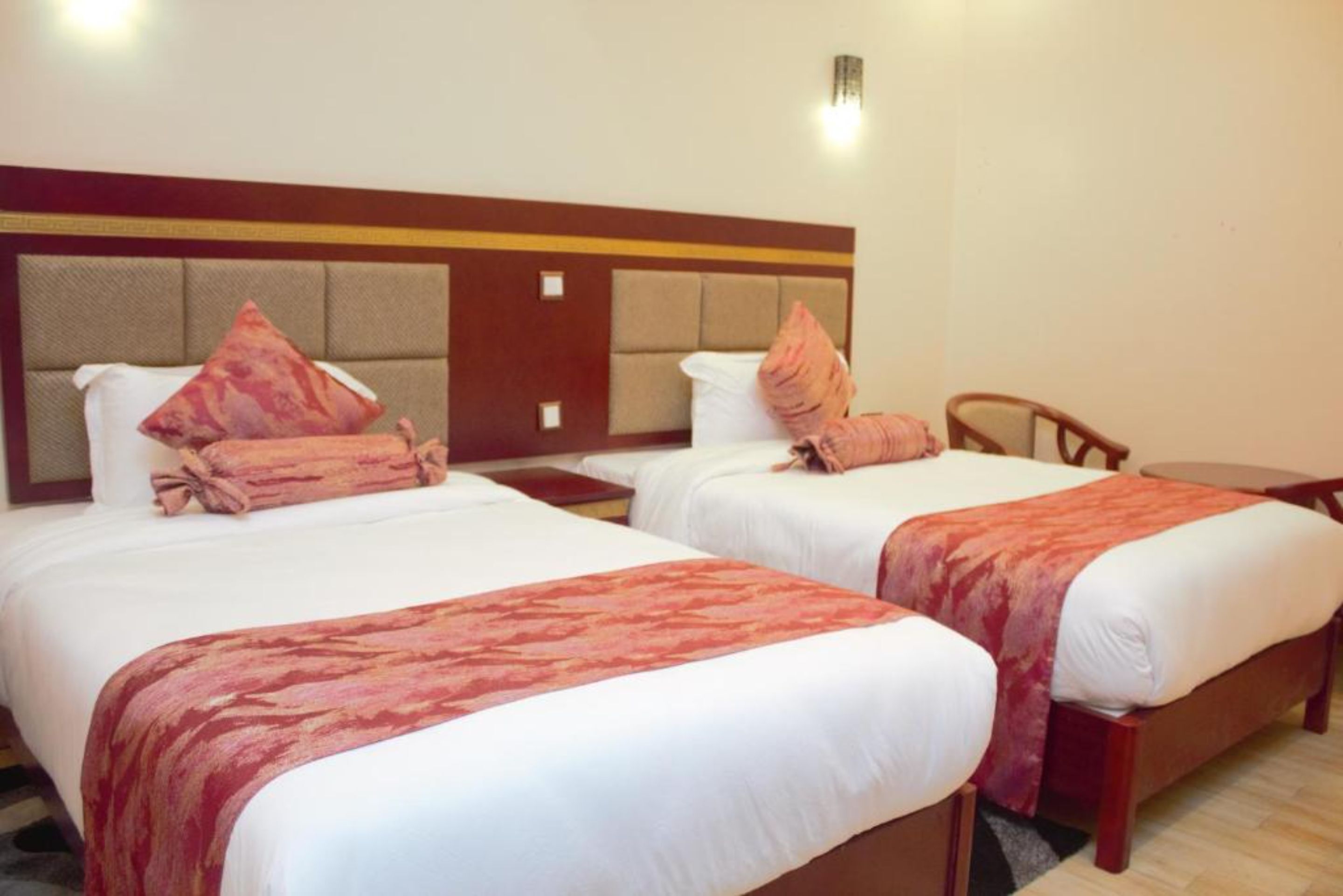 A hotel room with two beds, each with a red and white bedspread, and a wooden headboard. There is a small table and a chair in the room.