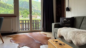Ein Wohnzimmer mit einer Couch, einem Holztisch, einem Kuhfellteppich und Blick auf Berge durch eine Schiebeglastür.