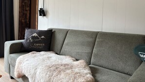 Ein graues Sofa mit einer flauschigen weißen Decke und einem Kissen mit Bergbild.