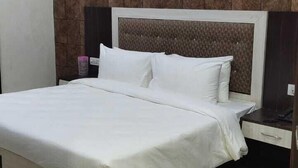 A neatly made bed with white linens, a headboard with a textured pattern, and a nightstand with a lamp. - Green Leaf (Jhansi)
