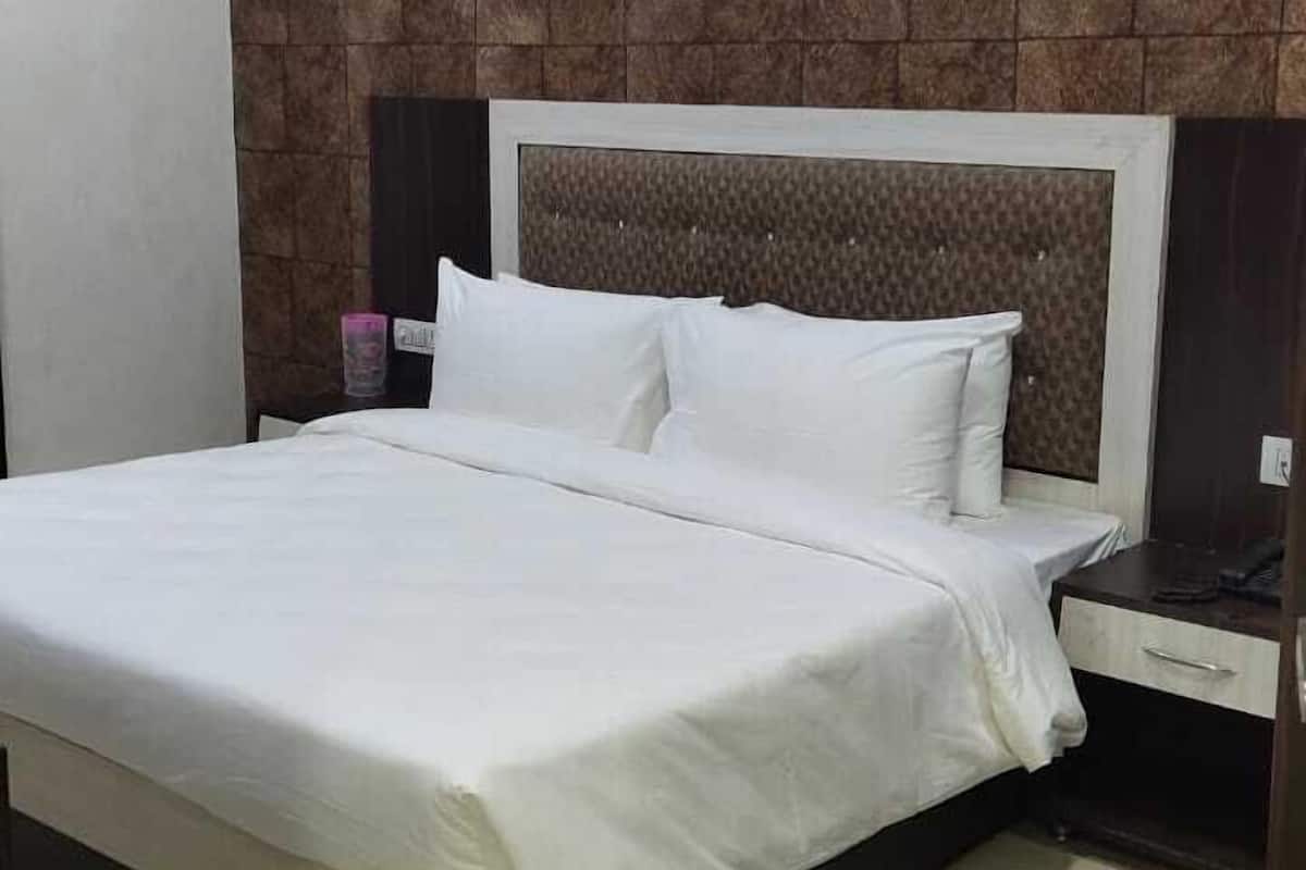 A neatly made bed with white linens, a headboard with a textured pattern, and a nightstand with a lamp.