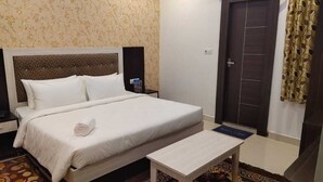 A neatly made bed with white linens, a wooden headboard, a bedside table, and a patterned rug. - Green Leaf (Jhansi)