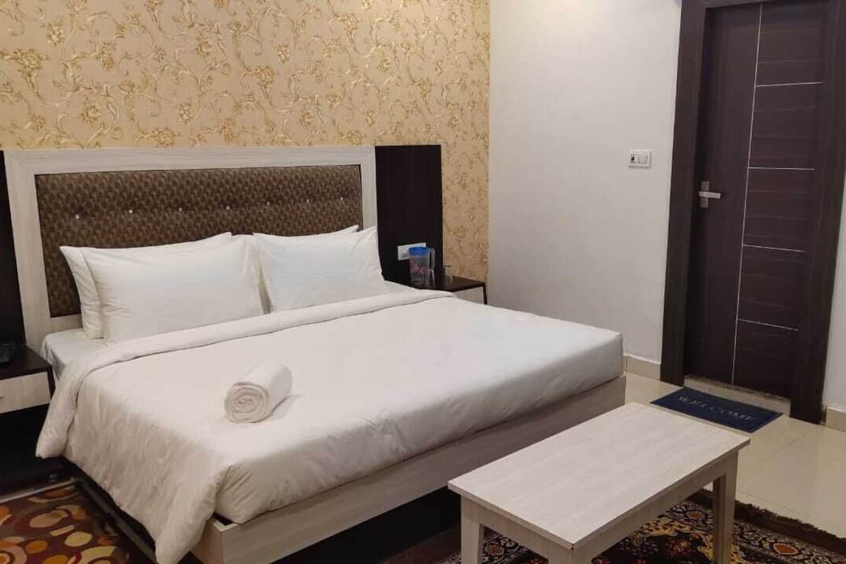 A neatly made bed with white linens, a wooden headboard, a bedside table, and a patterned rug.