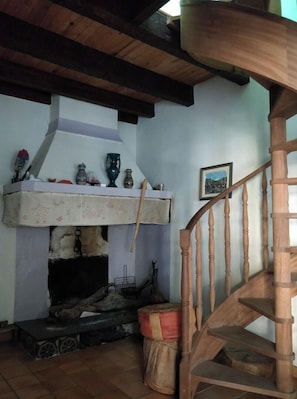 A rustic interior with a wooden staircase, a fireplace, and a shelf with various items. - Family winegrower's house (Roquebrun)