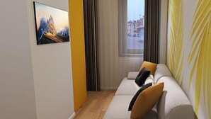 Ein modernes Hotelzimmer mit Sofa, einem Gemälde an der Wand, einem Fenster mit Blick auf Gebäude und einem Vorhang.