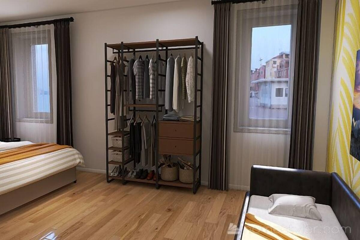 A hotel room with a bed, a wooden floor, a clothing rack, and a window with a view of buildings.