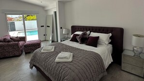 Een moderne slaapkamer met een groot bed, twee nachtkastjes, een fauteuil en uitzicht op een zwembad.