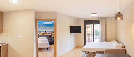 Ett hotellrum med en säng, ett skrivbord, en stol, en tv och utsikt över havet genom ett fönster.