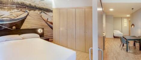 A bedroom with a large bed, wooden wardrobe, and a dining area with a table and chairs.