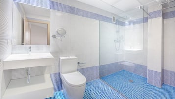 Ett modernt badrum med ett vitt handfat, toalett och duschhörna, med blå mosaikplattor på golvet och väggarna.