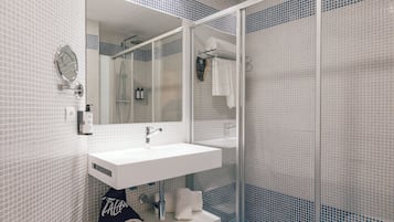 Ein modernes Badezimmer mit einem weißen Waschbecken, einem großen Spiegel und einer Duschkabine aus Glas.