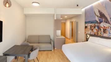 A modern hotel room with a bed, a sofa, a dining table, and a painting on the wall.